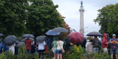 Des parisiens et des touristes sous la pluie qui regardent passer des cyclistes - le 27 juillet 2024